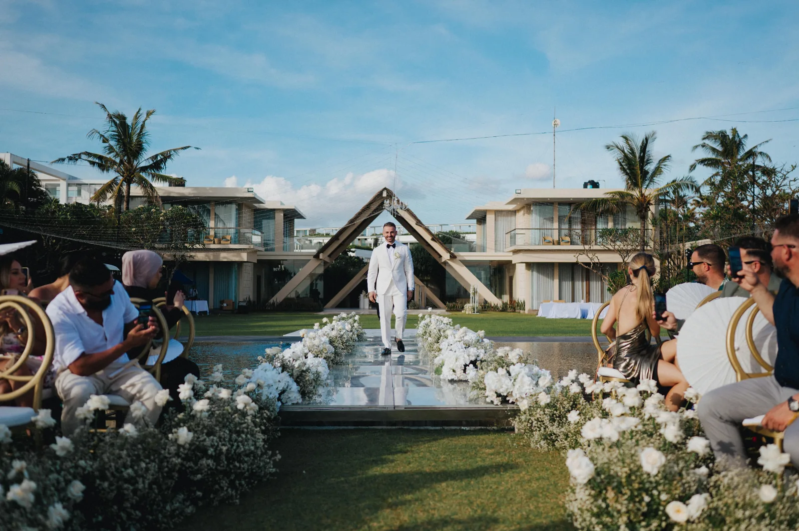 A ceremony on the lawn at Phalosa Villa, white florals lining the aisle and the villa behind